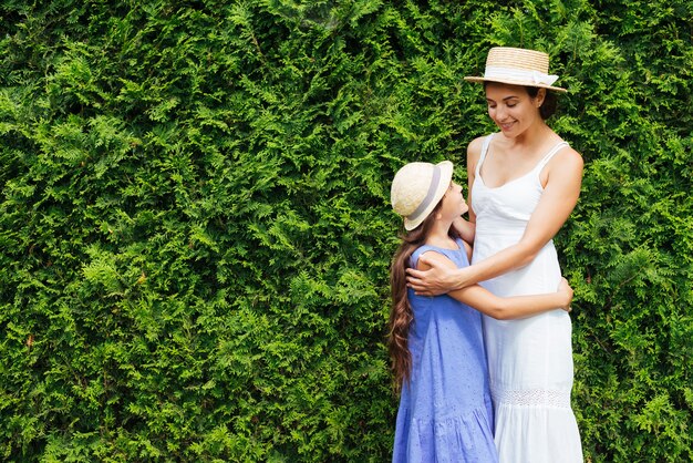 Mother and daughter hugging in front of bushes