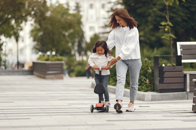 Mother and daughter on kick scooter in park. Kids learn to skate roller board. Little girl skating on sunny summer day.