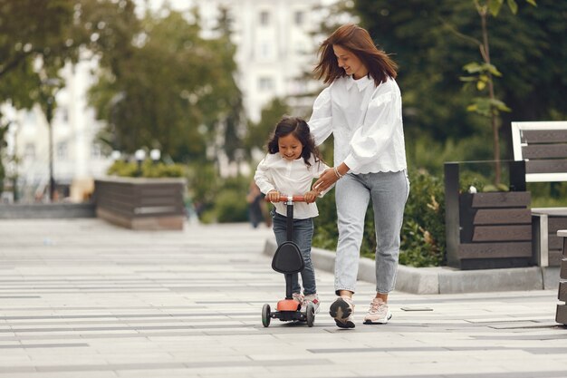 공원에서 킥 스쿠터에 엄마와 딸. 아이들은 롤러 보드 스케이트를 배웁니다. 화창한 여름 날에 스케이트 어린 소녀입니다.