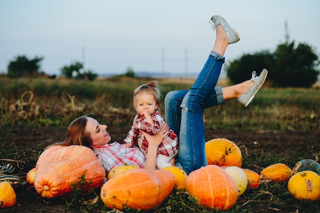 Free photo mother and daughter lie between pumpkins on the field, halloween eve