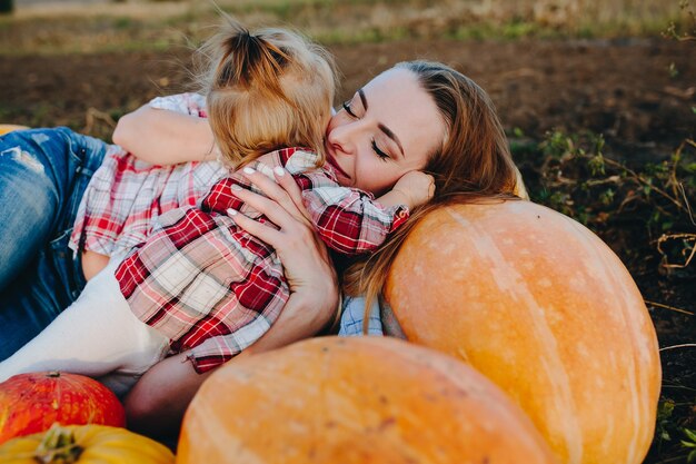 Free photo mother and daughter lie between pumpkins on the field, halloween eve