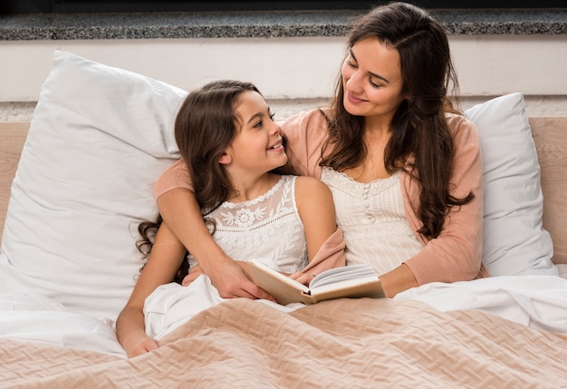 Мать и дочь читают книгу в постели