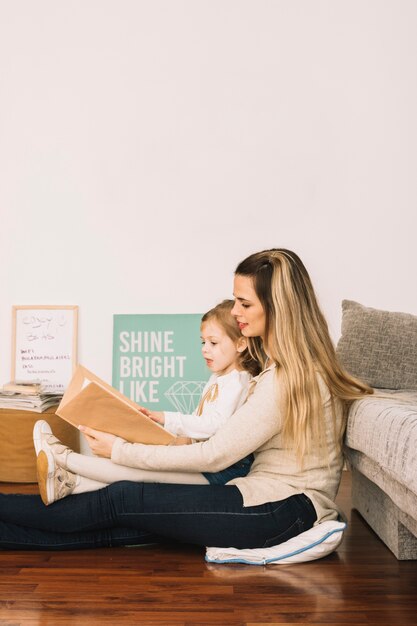 Mother and daughter reading book on floor