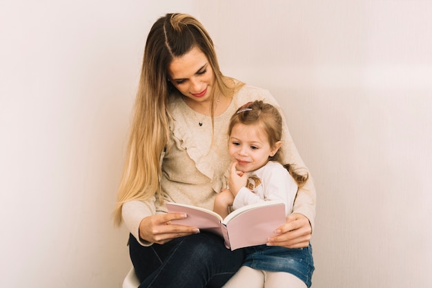 Foto gratuita libro di lettura della figlia e della madre vicino alla parete bianca