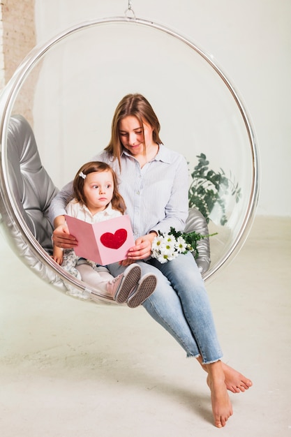 Mother and daughter reading greeting card in hanging chair 