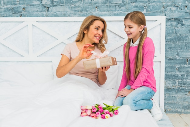 Free photo mother and daughter sitting on bed with gift box