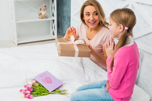 Mother and daughter sitting on bed with gift