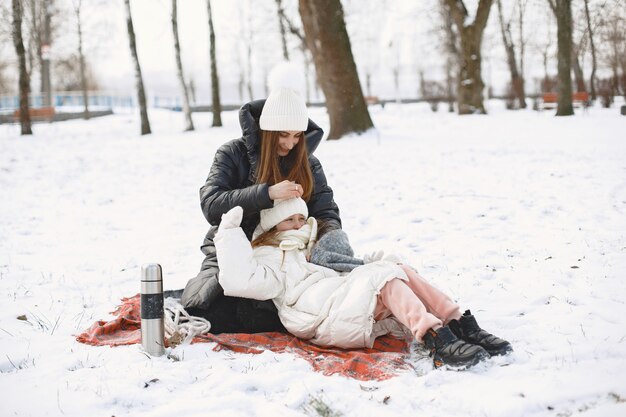 雪の公園の毛布に座っている母と娘