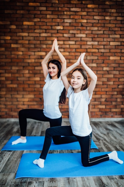 Free photo mother and daughter sitting in lotus pose at home and meditating together.