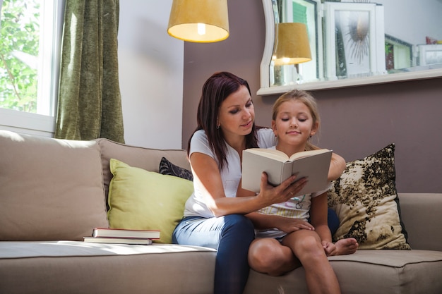 Mother and daughter sitting on sofa reading