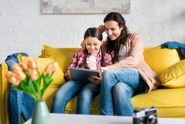 Mother and daughter sitting on yellow couch front view