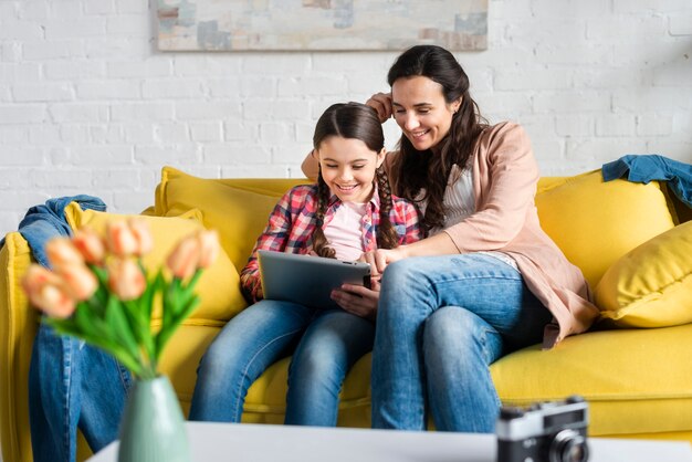 Mother and daughter sitting on yellow couch front view