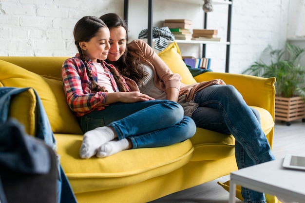 Mother and daughter sitting on yellow sofa