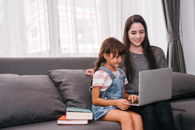 Mother and daughter spending time together in living room Mother teaching her daughter homeschooling online via laptop remote study elearning