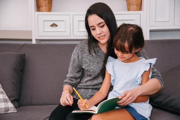 Mother and daughter spending time together in living room Mother teaching her daughter homeschooling reading a book study at home