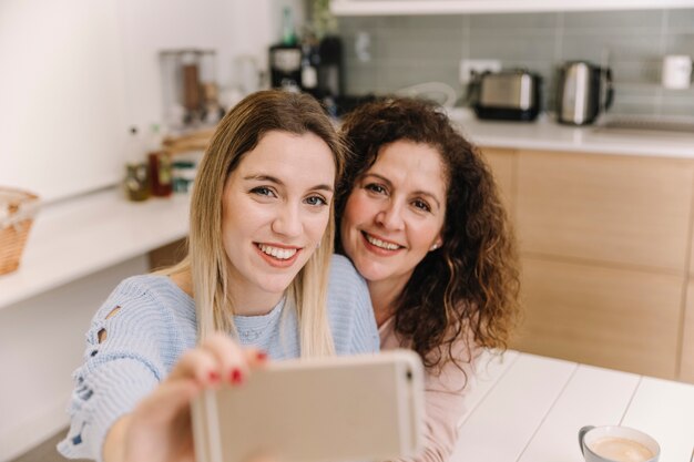 Mother and daughter taking selfie in kitchen