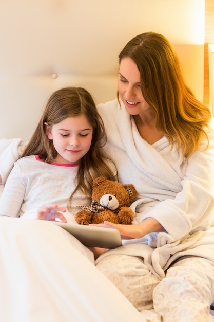 Mother and daughter using digital tablet in bedroom