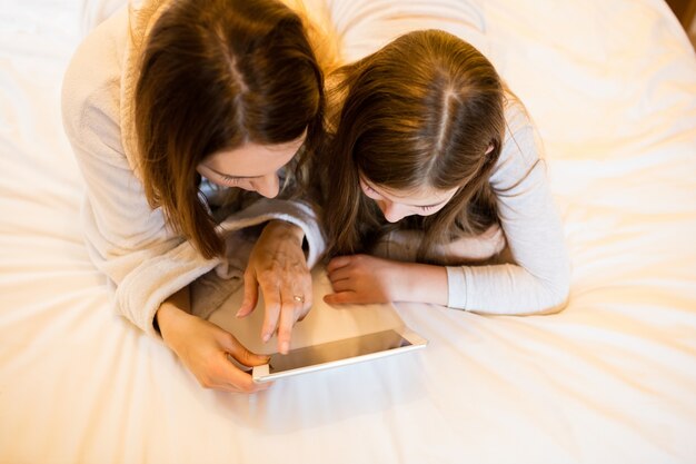 Mother and daughter using digital tablet in bedroom