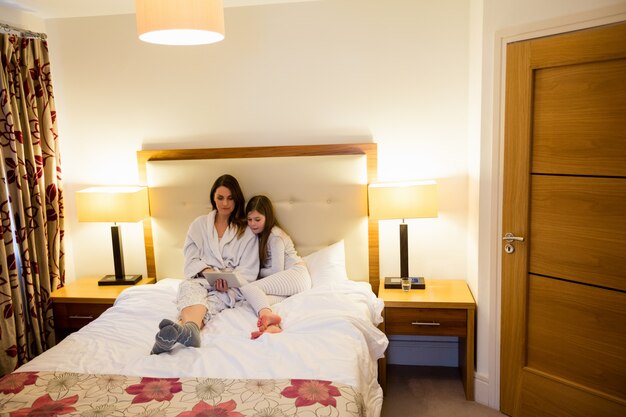 Mother and daughter using digital tablet in bedroom