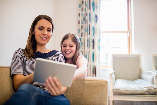 Mother and daughter using digital tablet in living room