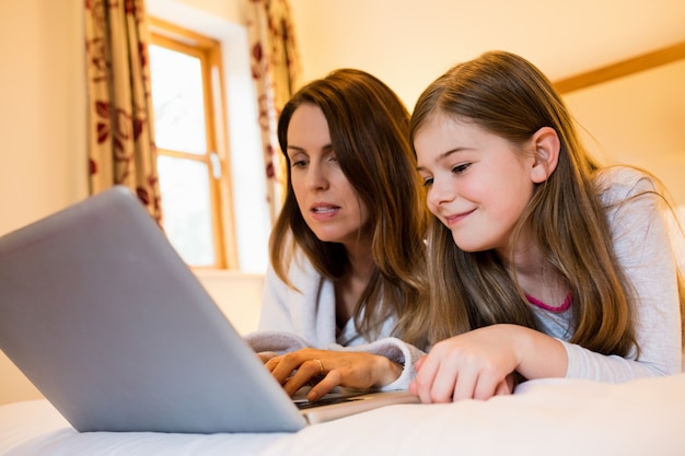 Mother and daughter using laptop in bedroom