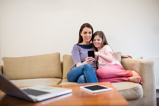 Mother and daughter using mobile in living room
