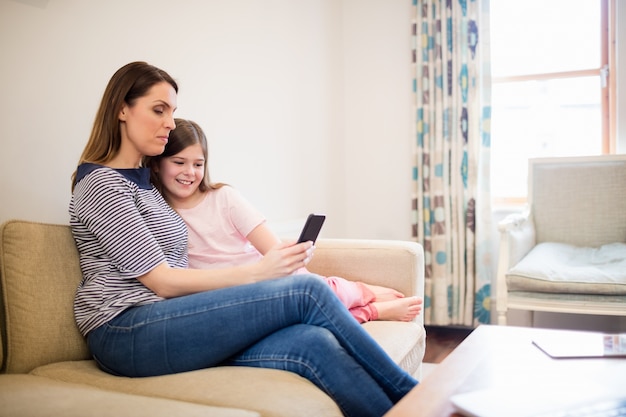 Mother and daughter using mobile in living room