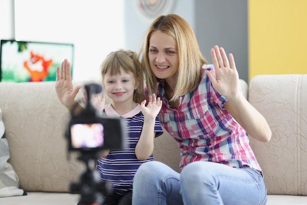 Mother and daughter wave hello on video videocamera set on tripod