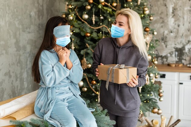 自宅でのお祝いの際、クリスマスツリーの下で医療用マスクを着用した母と娘。