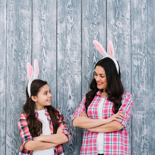 Mother and daughter with arms crossed looking at each other against wooden gray backdrop