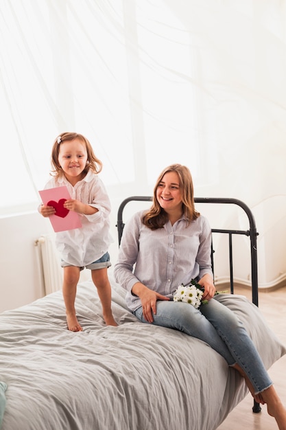 Mother and daughter with greeting card on bed