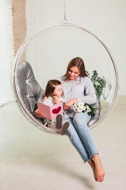 Free photo mother and daughter with greeting card in hanging chair