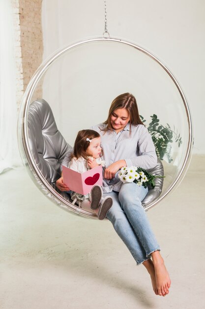 Mother and daughter with greeting card in hanging chair 