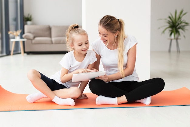 Mother and daughter on yoga mat at home playing on tablet