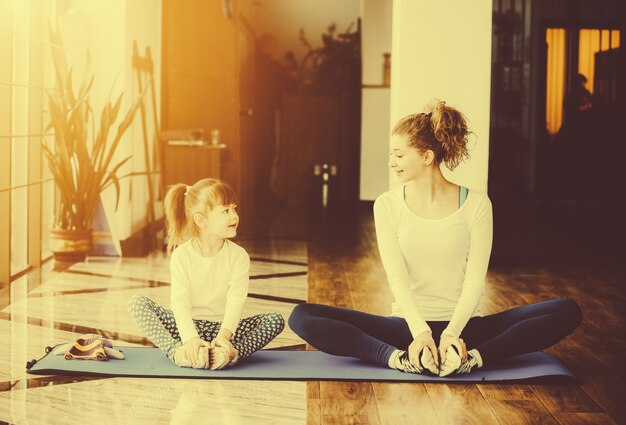 Mother and daughter in yoga pose sitting on a mat