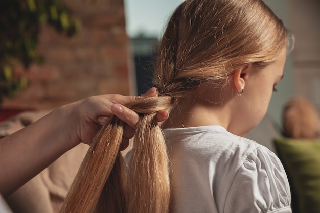Мать заплетает волосы дочери в косички