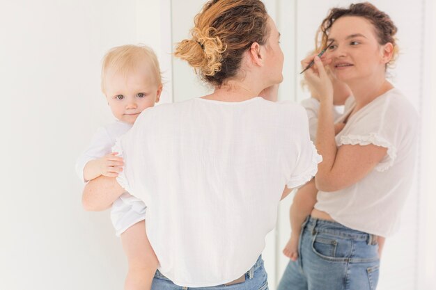 Mother doing her make-up while holding baby girl