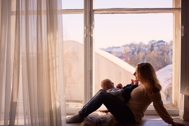 The mother embrace her son and sit on the window sill