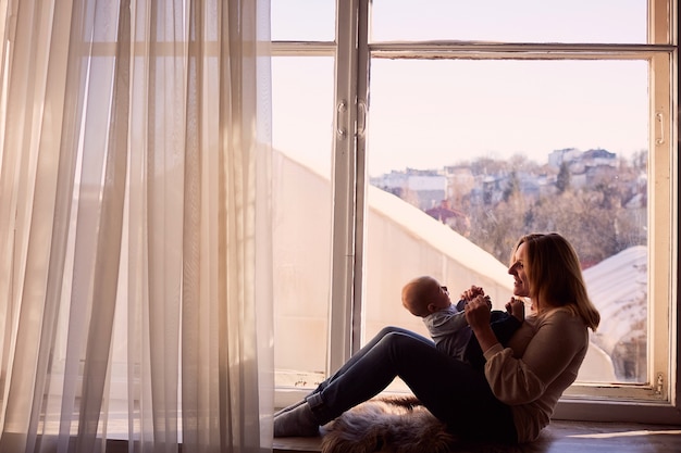 Mother embraces her son and sits by the window