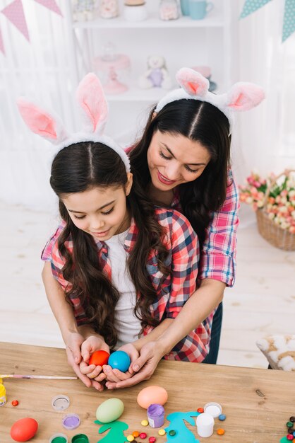 Mother embracing her daughter holding red and blue eggs on easter day