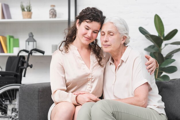 Mother embracing her senior mother sitting on sofa at home