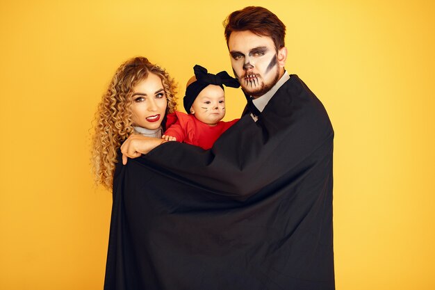 Mother father and children in costumes and makeup. People standing on a yellow background.