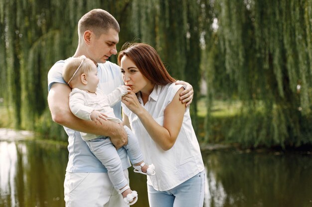 Mother, father and little baby daughter standing in the park and posing for a photo. Family wearing white and light blue clothes