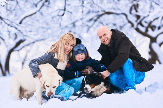 The mother, father, son and dogs sitting on the snow