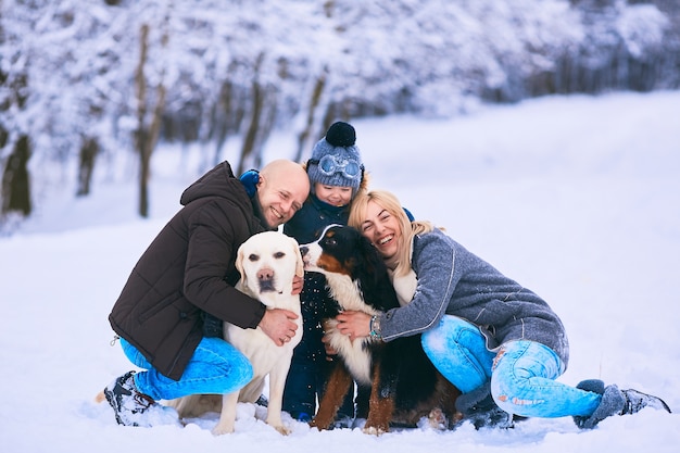 The mother, father, son and dogs sitting on the snow