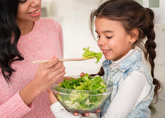 Mother feeding daughter salad