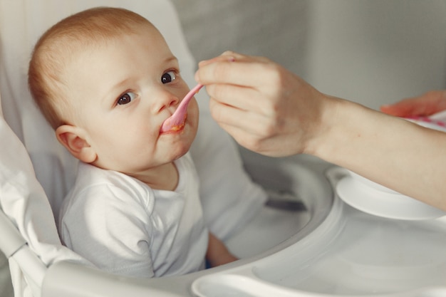 Free photo mother feeding her little baby in a kitchen