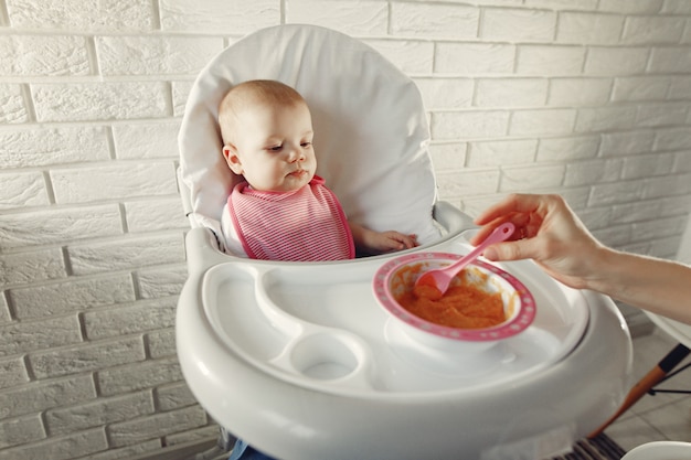 Free photo mother feeding her little baby in a kitchen