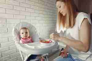 Free photo mother feeding her little baby in a kitchen