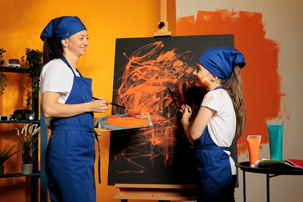 キャンバスにオレンジ色の絵の具を使った母と女の子、水彩のアクアレルで芸術的な傑作を描き、パレットとブラシからぬれた絵の具を描きます。スキルと創造的なビジョンでカラフルなアートワークを作成します。